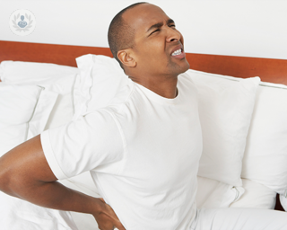 Man getting out of bed holding his lower back in pain