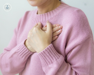 A woman holding both of her hands to her chest due to feeling heartburn.