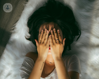 A young woman lying on the floor, covering her face with her hands