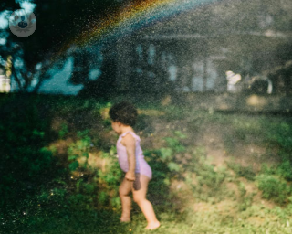 A child playing alone while a rainbow arcs over her