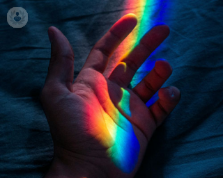 A rainbow light shines on an upside palm with the finger curling in