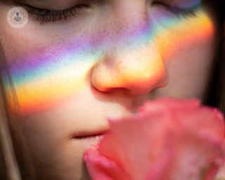 A young woman smells a flower, her sense of smell unimpaired by her less invasive rhinoplasty