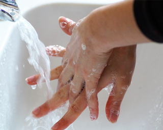 A pair of woman's hands. They are being washed thoroughly under a tap with soapy water.
