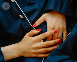 A woman holds her hands to abdomin in pain. Her nails are orange.