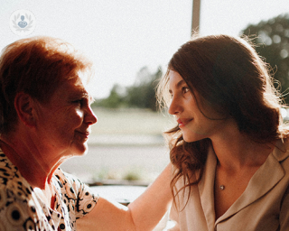 An elderly woman and her daughter, smiling at each other