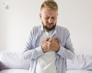 A young man holding both of his hands to his upper chest, experiencing acid reflux.