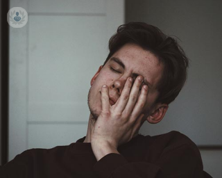 A young man holding his left hand to his face, with his eyes closed.