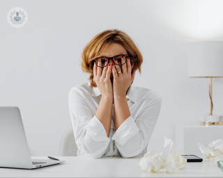 A women at a desk hiding her face between both her hands, feeling stressed