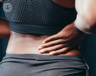 A woman holding a hand to her lower back, feeling pain