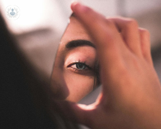 A woman looks at the camera through a reflection from a piece of mirror with only one eye