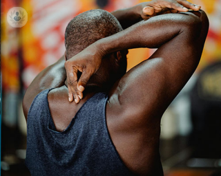 a man's back, he is flexing and stretching his arms behind his head, accentuating his shoulder