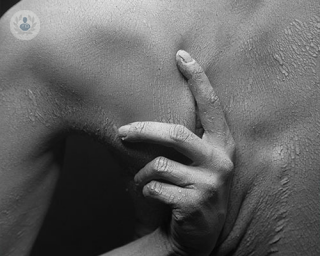 A person reaching to scratch their back which is apparently dry and scaly. The photo is in black and white.