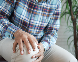 An elderly man holding both his hands to his right knee, due to osteoarthritis.