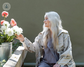 An older woman sits in a beautiful garden and caresses a flower