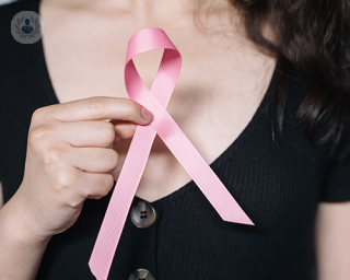 A young woman holding a pink breast cancer ribbon.