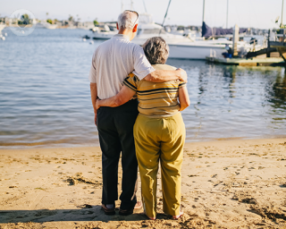 An elderly couple hugging each other, looking out into the sea.