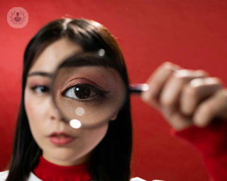 A woman holds a magnifying glass to her eye, enlargening it. She is examining the risks of myopia