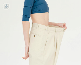 A woman compares her current size wearing a pair of trousers that are too large