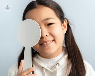 A little girl in pigtails covers one eye with a white paddle and smiles at the camera