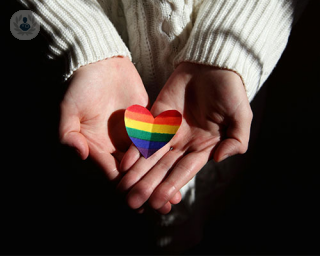 A pair of hands hold out a rainbow heart from the darkness