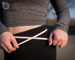 Woman measuring her waist, debating about getting a gastric balloon or gastric band