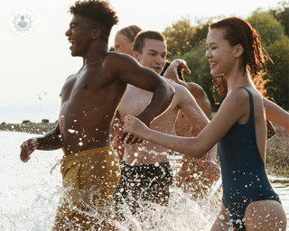 A group of diverse youths run into a lake, laughing and carefree