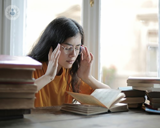 A young woman with a hormonal headache, holding both of her hands to her temple.