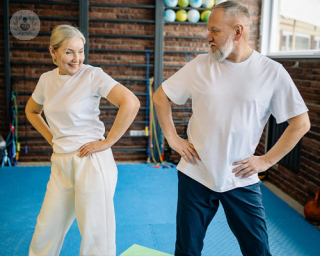 Two elderly people smile and dance, shaking their hips