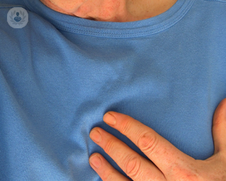 An elderly man holding his left hand to his heart, feeling chest pain.