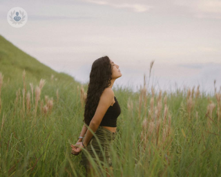 A young woman stands in a field and breathes deeply, tilting her head back