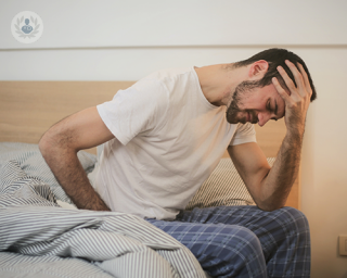 A young man sitting on his bed, bent over in pain