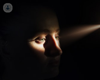 Woman with diabetes that might lead to blindness in a dark room with light shining on her eyes and nose