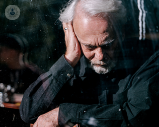 An elderly man pressing his right hand onto his right ear