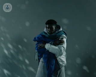 A man hugs himself against a cold, snowy backdrop