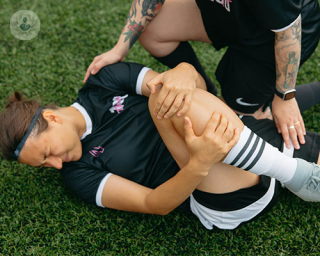 A football player lies on the field in agony after her mensicus cartilage has torn, her fellow players standing over in concern