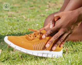 A person with an ankle sprain, holding their left ankle with both of their hands.