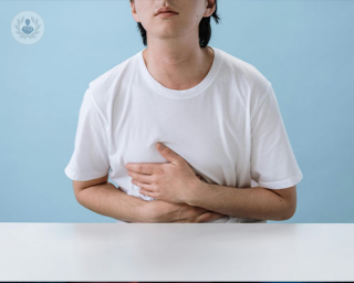 A man holds his stomach in pain, possibly experiencing acid reflux