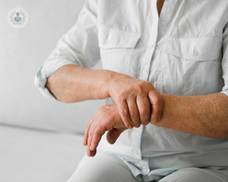 A man holding his left wrist with his right hand, feeling joint pain. His hands are both red and inflamed.