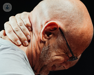 An elderly man holding the back of his neck in pain.