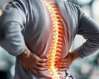 A man holding both of his hands to his lower back, feeling pain due to a herniated disc.