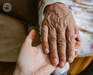 An elderly woman with hand arthritis laying her hand on top of another person's hand.