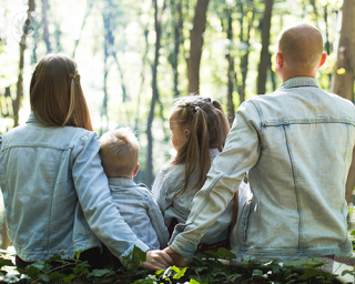 A family of 4 sitting in the forest floor, looking out to the trees in front.