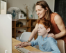 A mother at a desk looking at a computer which shows her son's homework.