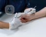 A surgeon stitching a patient's base of the thumb.