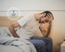 A tired man sitting on his bed.