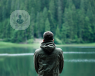 The back of a young man staring at a lake.