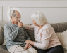 An elderly man sat on a sofa coughing into his right fist, with his wife next to him looking with concern.