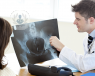A doctor is holding up an x-ray image of the hip region. He is pointing to it and explaining it to a patient.