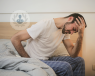 A young man bent over on his bed due to feeling pain.