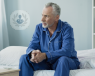 A man sitting anxiously at the end of a hospital bed. 